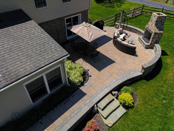Aerial of a Garnet Valley back patio — curved paver platform, in-ground hot tub, full-height fieldstone outdoor fireplace — Nature's Call Landscaping