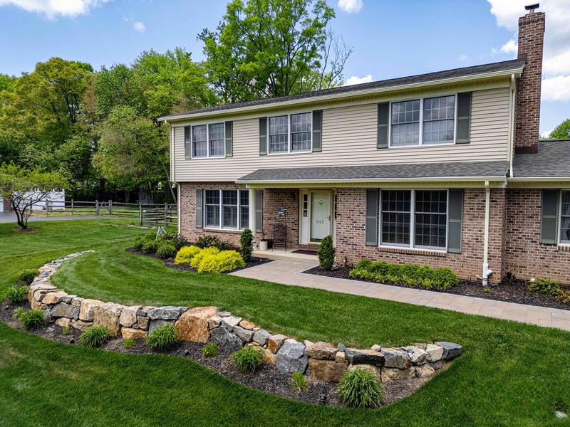 Garnet Valley Pennsylvania outdoor patio at evening — stone seat wall, paver platform, and ambient lighting accenting the architecture and plantings — Nature's Call hardscape and lighting project