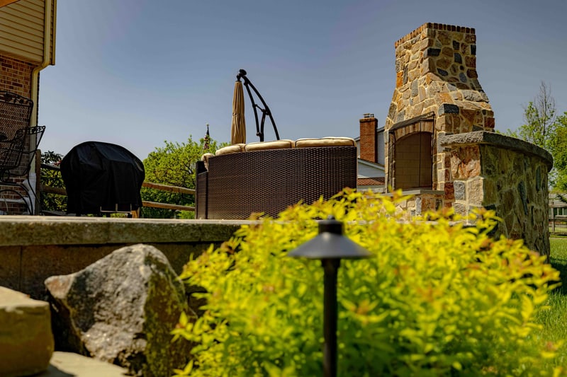 Low-angle view of the Garnet Valley fieldstone outdoor fireplace and in-ground hot tub, with a yellow-foliage shrub vivid in the soft-focus foreground
