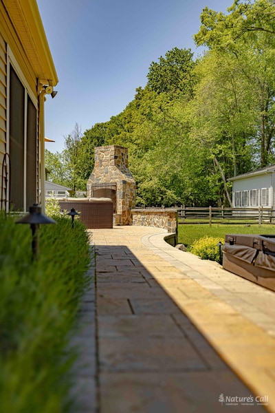 Long perspective view down the paver walkway alongside the Garnet Valley home, leading the eye to the full-height fieldstone outdoor fireplace at the path's end