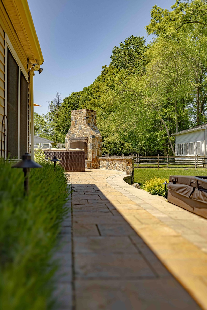 Long perspective view down the paver walkway alongside the Garnet Valley home, leading the eye to the full-height fieldstone outdoor fireplace at the path's end