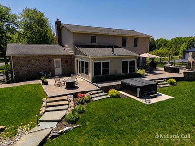 Elevated view of the rear of the Garnet Valley home, showing the multi-level paver patio with dining set, the in-ground hot tub, and stone steps leading down to the lawn