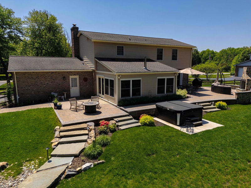 Elevated view of the rear of the Garnet Valley home, showing the multi-level paver patio with dining set, the in-ground hot tub, and stone steps leading down to the lawn