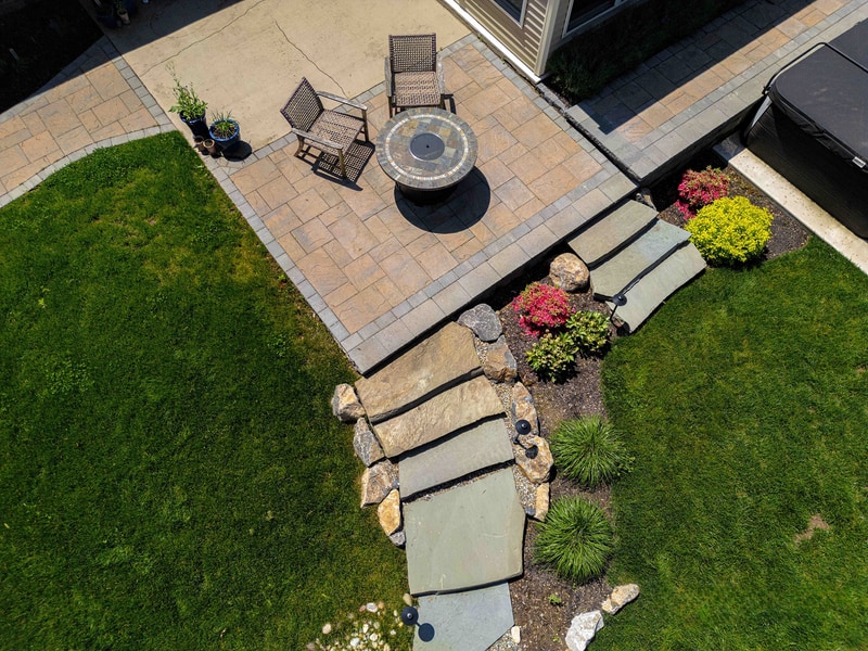 Aerial view of the Garnet Valley fire pit area, showing the curved seating arrangement, paver patio, and transition to the lawn through stone-edged plant beds
