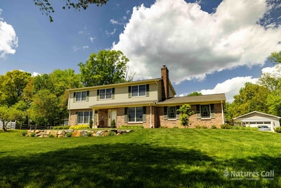 Head-on view of the Garnet Valley two-story brick and cream-siding home from across the lawn, with dramatic cumulus clouds filling the blue sky above the freshly landscaped front yard