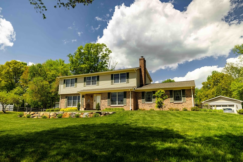 Head-on view of the Garnet Valley two-story brick and cream-siding home from across the lawn, with dramatic cumulus clouds filling the blue sky above the freshly landscaped front yard
