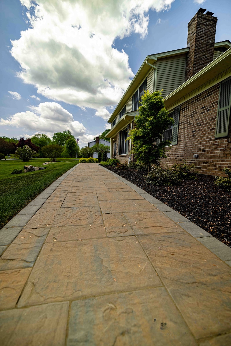 Low-angle view of the Garnet Valley front paver walkway leading toward the home's entry, with dramatic storm clouds overhead and a tall tree silhouetted on the right
