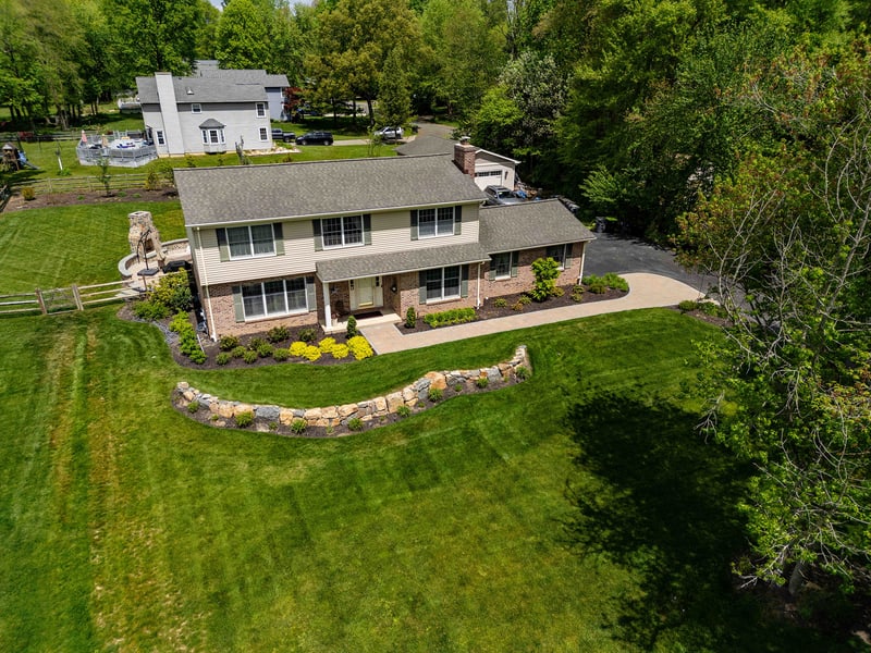 Aerial angled view of the full Garnet Valley property: the curved fieldstone retaining wall traces the front lawn edge, the paver walkway leads to the entry, and mature trees surround the back yard
