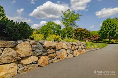 A maintained landscape and natural-stone retaining wall on a Greenville property — Nature's Call Landscaping