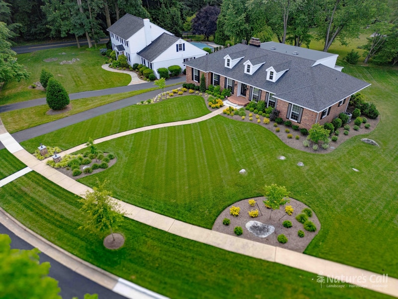 Aerial view of the completed Greenville, Delaware landscape transformation — brick lamp pillar entry, curved walkway, layered front beds, and natural stone retaining wall by Nature's Call Landscaping