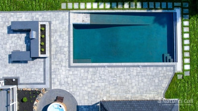 Overhead view of rectangular lap pool with paver deck, integrated spa, and geometric stone patio with lush lawn borders.