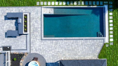 Overhead view of rectangular lap pool with paver deck, integrated spa, and geometric stone patio with lush lawn borders.