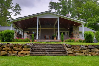 Brick pavilion with white columns and modern pitched roof, flanked by stacked stone retaining walls and manicured hedges lining the lawn.