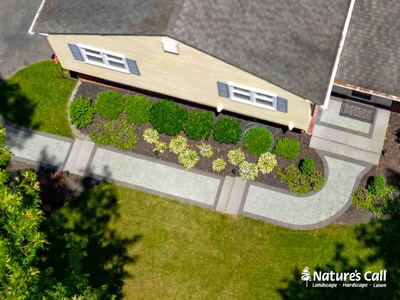 Aerial view of curved stone walkway with foundation plantings bordering residential home driveway and lawn.