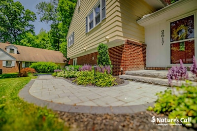 Curved paver entrance walkway with surrounding perennial plantings and flowering shrubs leading to brick home entrance.
