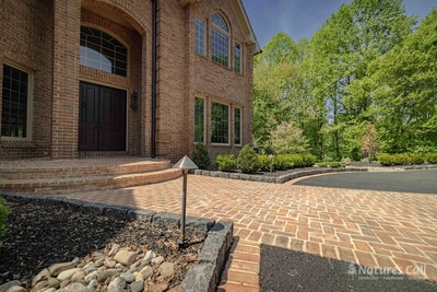 Ground-level shot of the Hockessin side garden: irregular flagstone steppers thread through a mulched bed in the foreground, with mounded boxwoods and small shrubs receding into a river-rock drainage strip and the home wall on the left