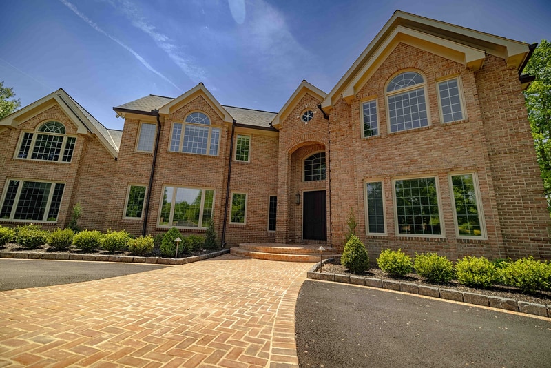 Detail view of the Hockessin entry walkway: a curved cobble edge defines the boundary between the brick paver path and a mulched bed of mounded boxwoods, with the brick step landing visible at the top of the frame