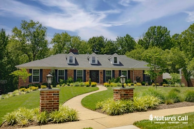 Curved driveway with ornamental grasses and foundation plantings framing brick colonial home in Greenville, DE.