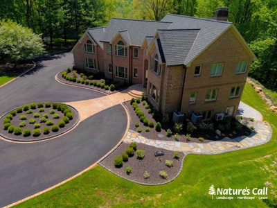 Brick colonial in Hockessin, DE features curved asphalt driveway with ornamental grass bed, stone accent borders, and foundation plantings.