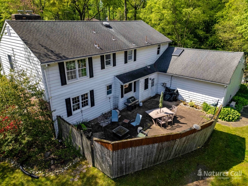 Before. Aerial view of the original North Wilmington back yard: a small weathered concrete patio sits behind the home with a low stockade fence ringing the yard, a small fire pit, and a mix of mismatched lawn chairs and a folding table on the slab